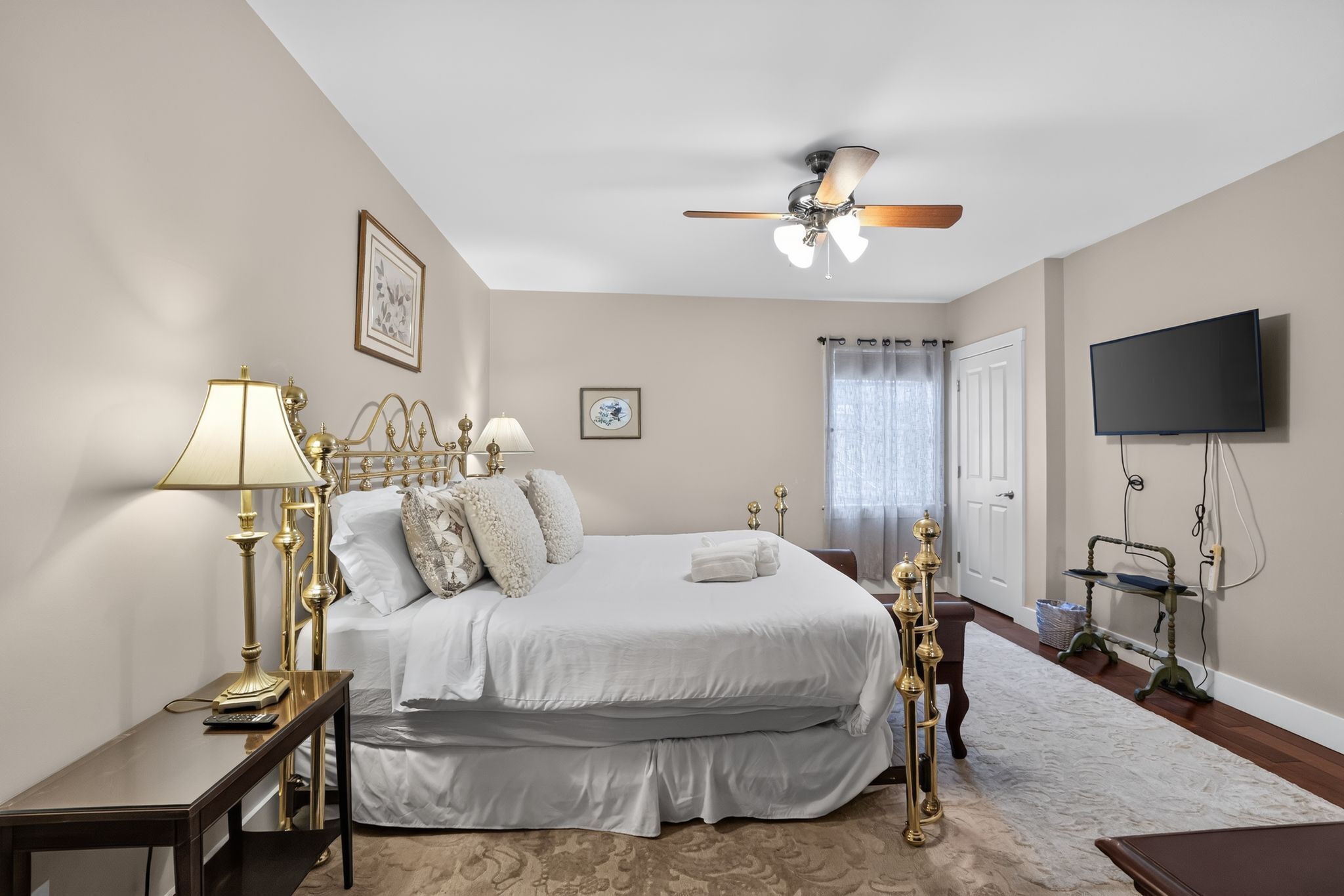 A hotel bedroom with a bed, bedside lamps, a ceiling fan, a television, and a window with curtains.
