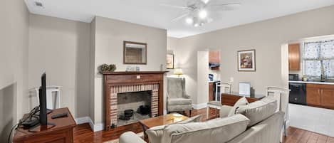 A living room with a fireplace, a sofa, a television, and a ceiling fan.