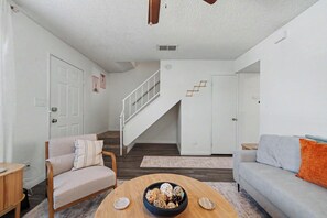 A modern living room with a sofa, a coffee table with decorative items, a staircase, and a door leading to another room. - Quiet 2BR Retreat Fast Wi-Fi Near Dining & Shops (Bakersfield)