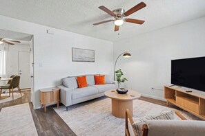 A modern living room with a sofa, coffee table, TV, and ceiling fan. - Quiet 2BR Retreat Fast Wi-Fi Near Dining & Shops (Bakersfield)