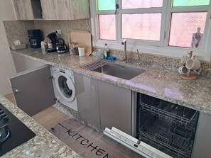A compact kitchen with a built-in washing machine, a sink, and a dishwasher.