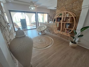 A modern living room with a stone wall, a wooden bookshelf, a white armchair, and a large vase.