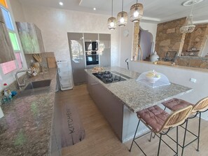 A modern kitchen with granite countertops, a central island, stainless steel appliances, and pendant lighting.