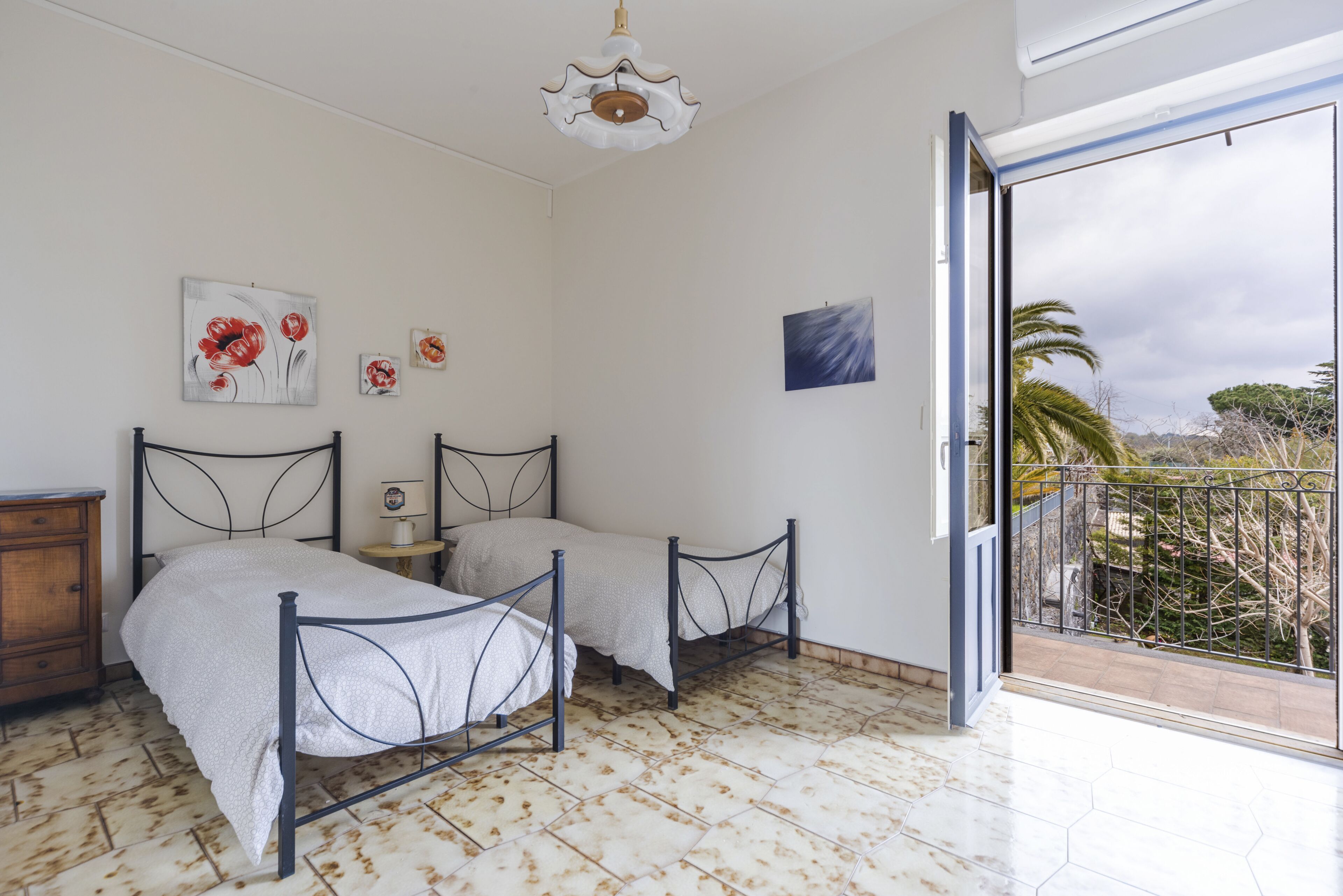 A bedroom with two beds, a small table, and a painting on the wall.