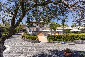 A stone pathway leading to a building with a pool, surrounded by greenery and outdoor seating. - Villa Etna Pool & Seaview by Wonderful Italy (Belpasso)