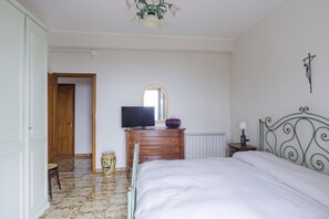 A bedroom with a bed, a dresser, a television, a mirror, a radiator, and a door leading to another room. - Villa Etna Pool & Seaview by Wonderful Italy (Belpasso)