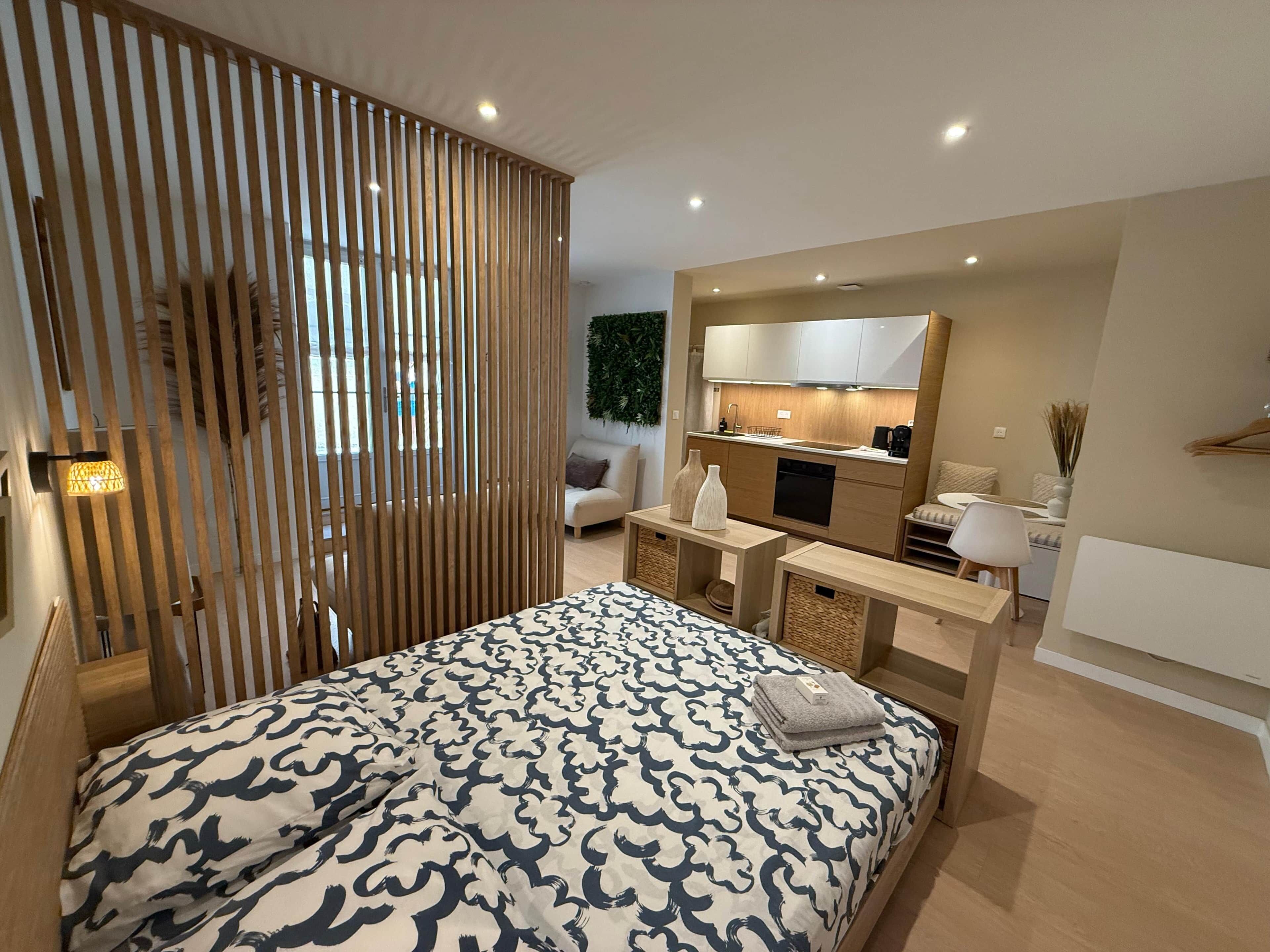 Une chambre moderne comprenant un lit, des tables de chevet, une petite kitchenette et une cloison coulissante en bois.