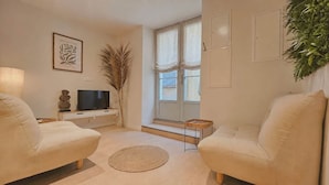 A living room with two sofas, a TV, a plant, and a window with curtains. - La Bohème - Historic City Centre Studio – Aix Cours Mirabeau (Aix-en-Provence)