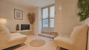 A living room with two sofas, a TV, a plant, and a window with curtains. - La Bohème - Historic City Centre Studio – Aix Cours Mirabeau (Aix-en-Provence)
