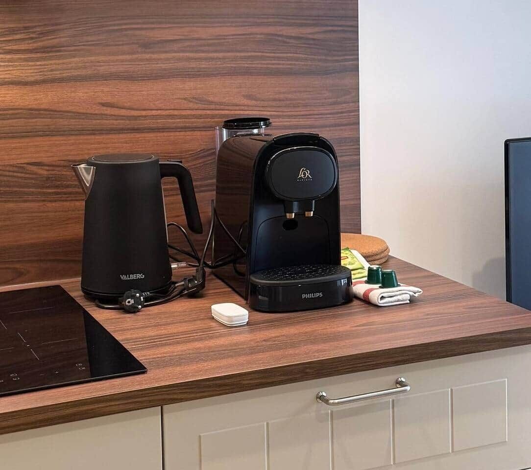 Una cocina con cafetera, hervidor y tostadora. Hay también condimentos y un pequeño electrodoméstico blanco en la encimera.
