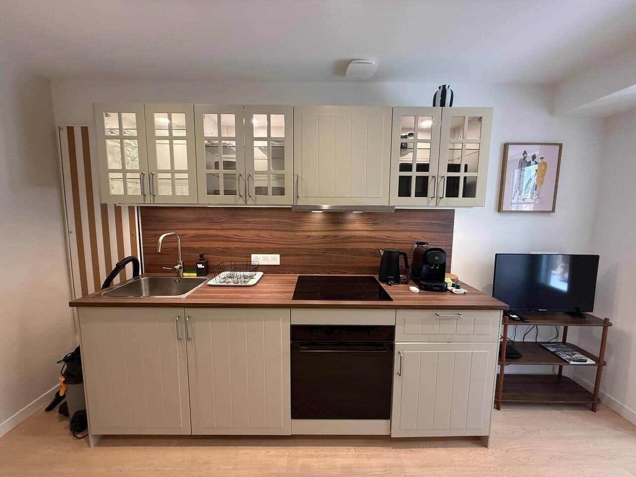 A compact kitchen with a built-in dishwasher, a coffee maker, and a television on a wooden stand.