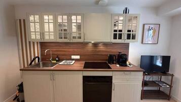 A compact kitchen with a built-in dishwasher, a coffee maker, and a television on a wooden stand.