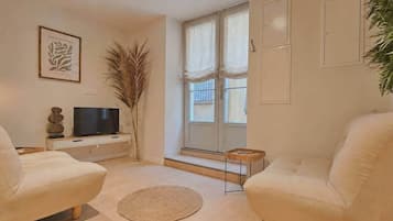 A living room with a sofa, a television, a decorative plant, and a window with curtains.