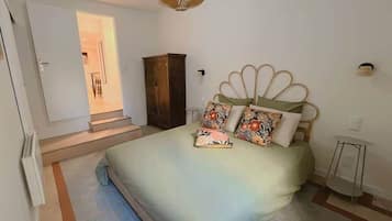 A bedroom with a bed, a wooden wardrobe, a small table, and a door leading to another room.