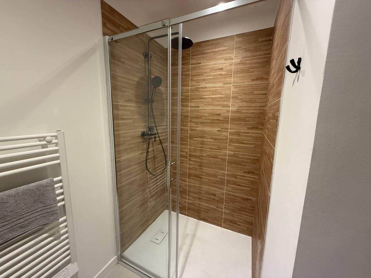 Una ducha con cerramiento de vidrio, pared de madera y radiador blanco.