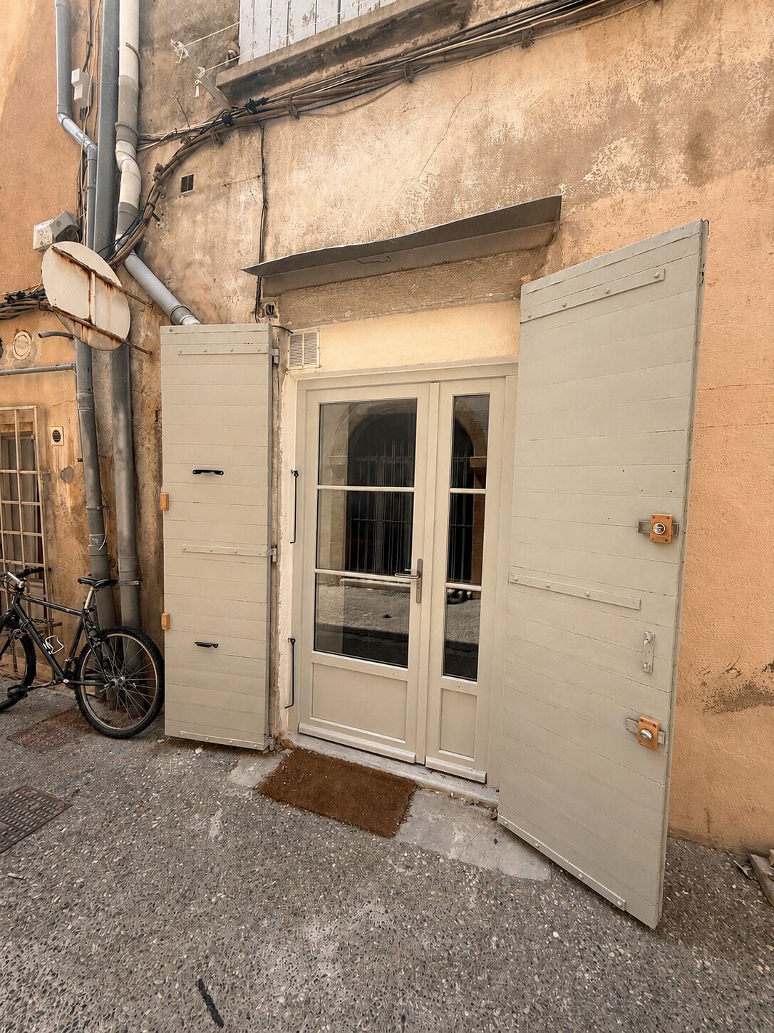A building with a large metal door, a bicycle parked outside, and visible pipes on the wall.