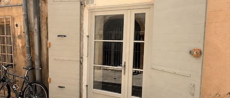 A building with a large metal door, a bicycle parked outside, and visible pipes on the wall.