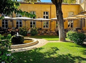 Ein Innenhof mit Außenbestuhlung, einem Brunnen und einem Gebäude mit vielen Fenstern.