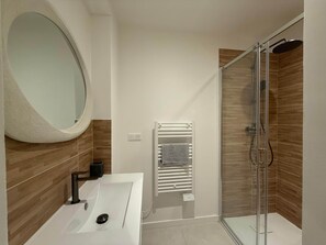 A modern bathroom with a glass shower enclosure, a white sink with a round mirror, and a towel rack. - L'échappée -Charming 1-Bedroom Apart in Aix Historic Center (Aix-en-Provence)