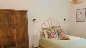 Quarto com guarda-roupa de madeira, cama com almofadas florais e luminária fixada na parede.