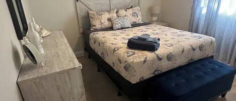 A bedroom with a bed, a nightstand, a dresser, a ceiling fan, and a window with curtains.