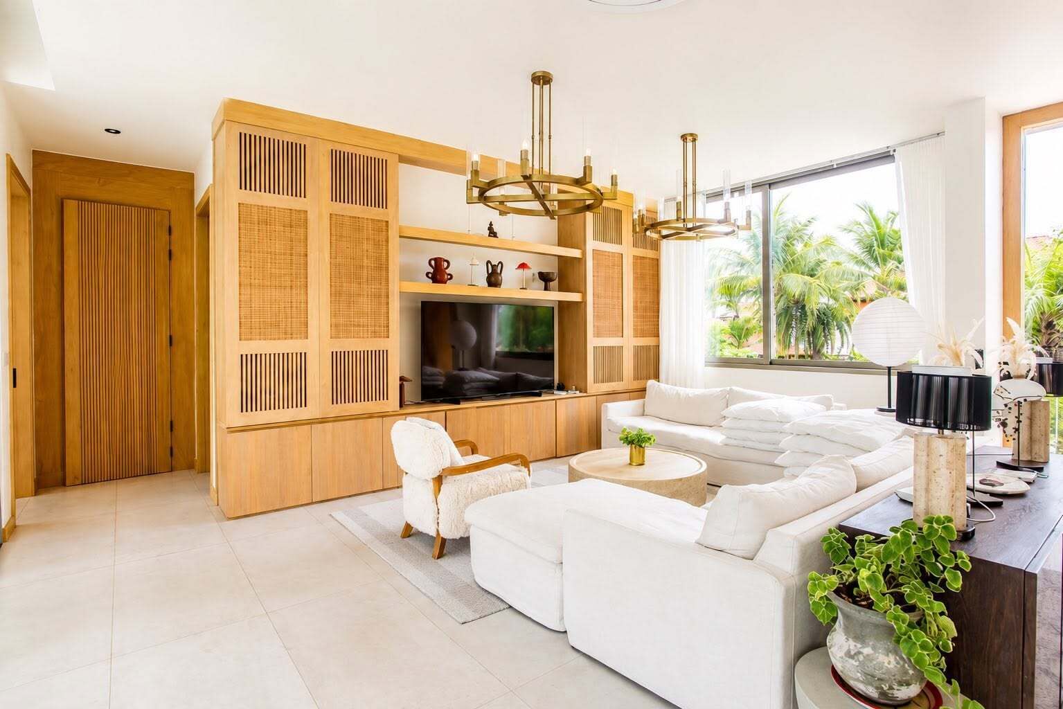 A modern living room with a sectional sofa, a television, and a large window with a view of palm trees.
