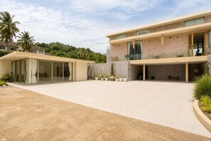 A modern two-story building with a covered patio area, large windows, and a view of a lush green landscape. - Exclusive Golf Villa at Plam Hill  (Cha-am)