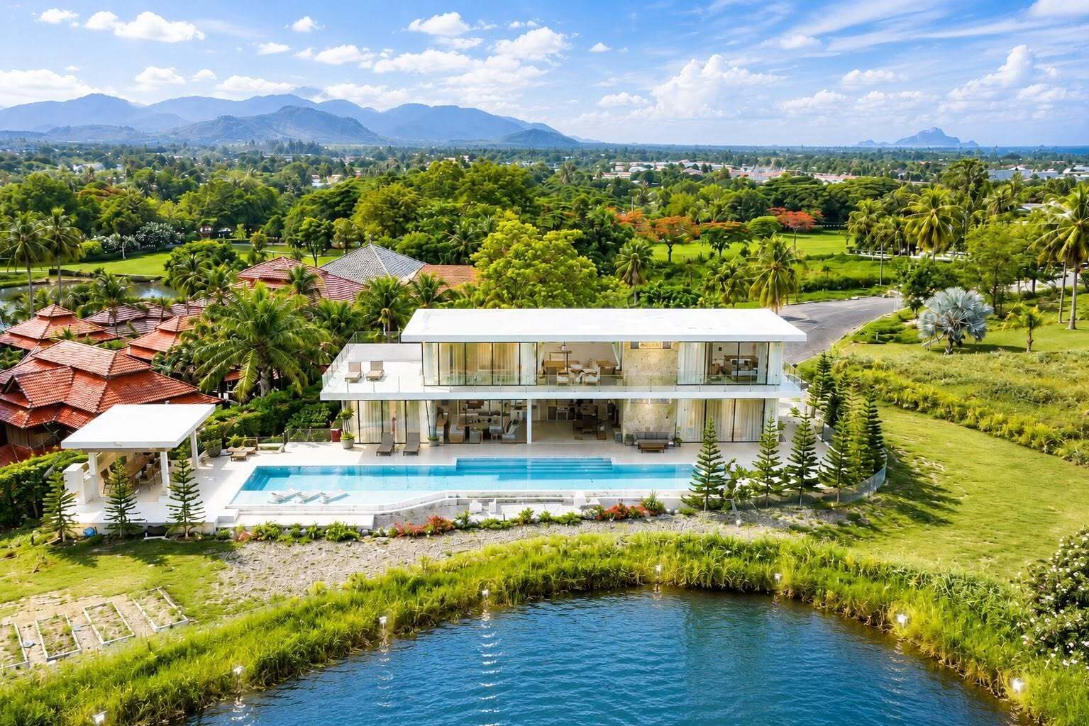 A modern two-story house with a swimming pool, surrounded by lush greenery and a view of distant mountains.