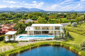 A modern two-story house with a swimming pool, surrounded by lush greenery and a view of distant mountains. - Exclusive Golf Villa at Plam Hill  (Cha-am)