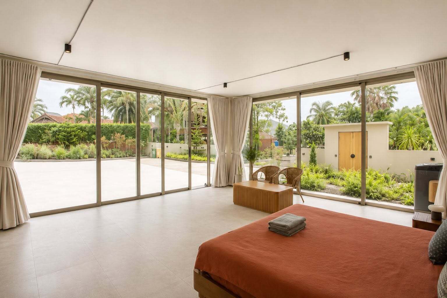 Un dormitorio con una cama grande, una zona de estar con sillas y vistas a un jardín y edificios.