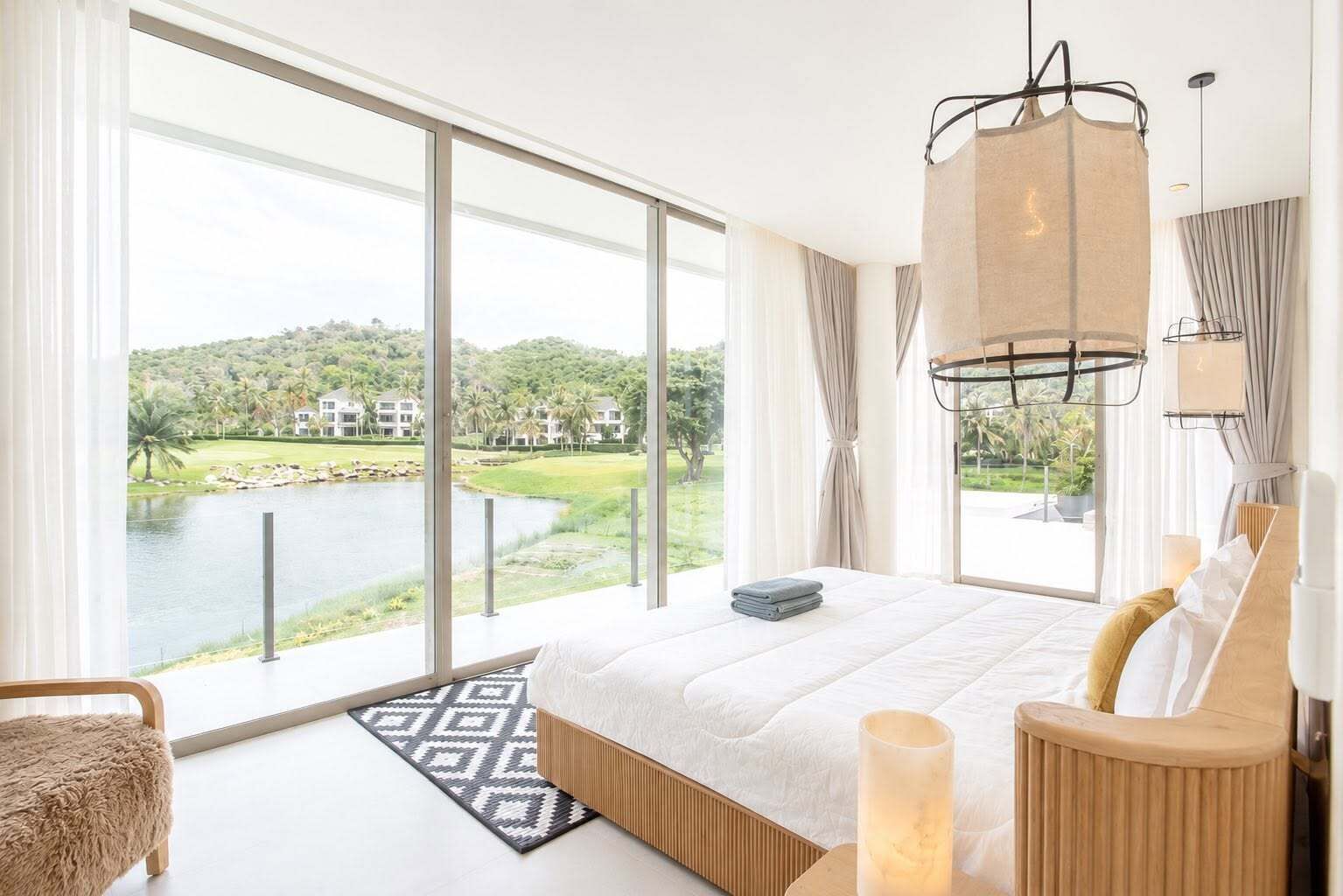 Un dormitorio con una cama grande, vista a un lago y una lámpara moderna.