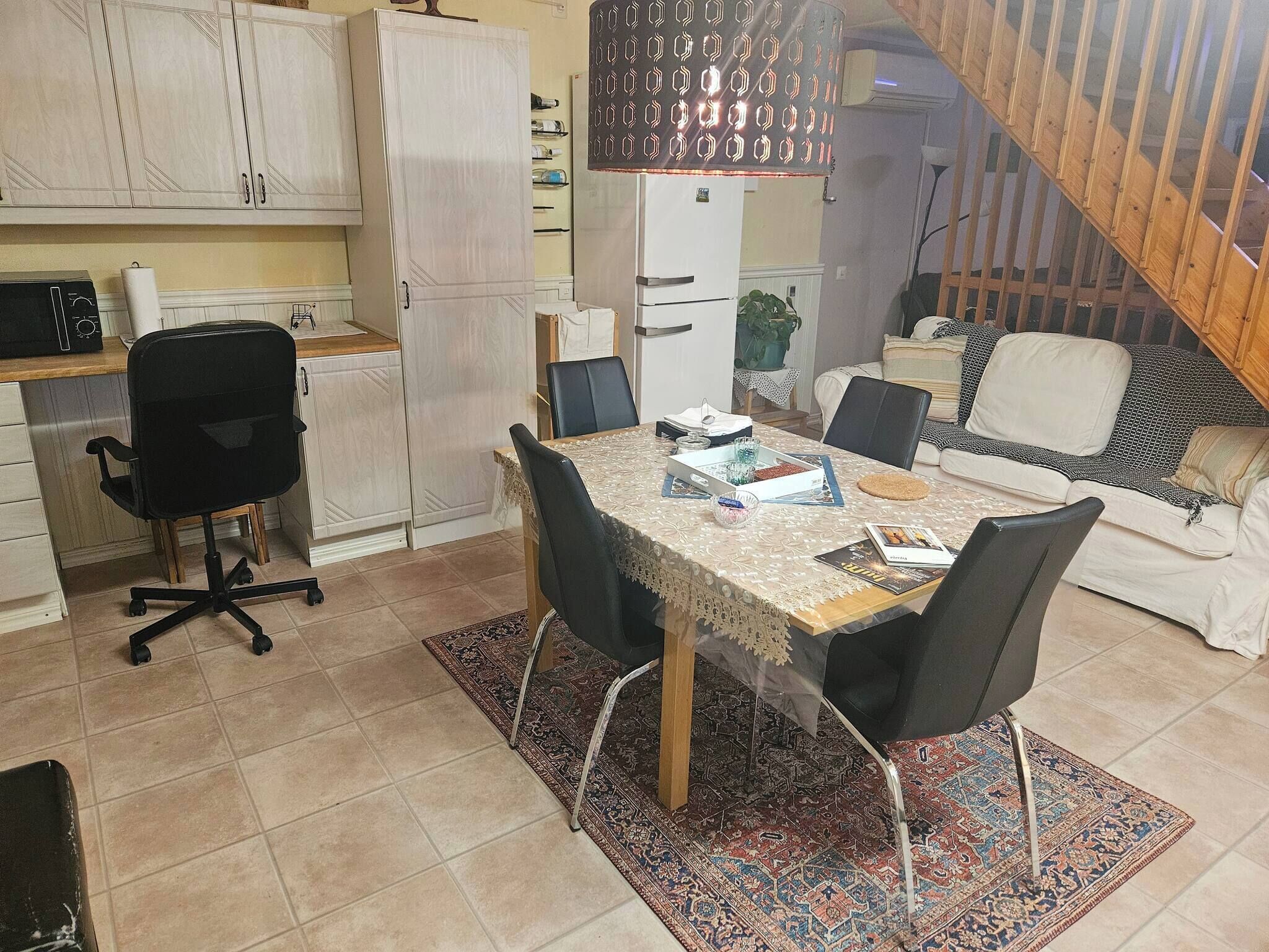 Un ambiente compatto con un tavolo da pranzo, sedie, un divano, un angolo cottura con pensili e una scala.