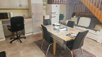 Un ambiente compatto con un tavolo da pranzo, sedie, un divano, un angolo cottura con pensili e una scala.
