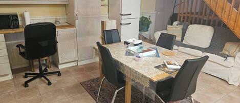 Un espace de vie compact comprenant une table à manger, des chaises, un canapé, un coin cuisine avec des placards et un escalier.