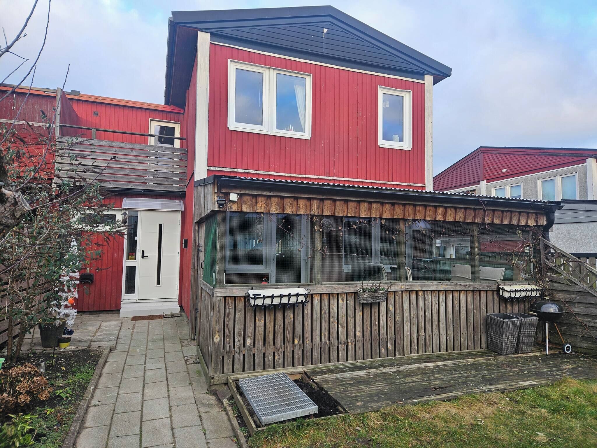 A red two-story house with a covered porch and a small garden area.