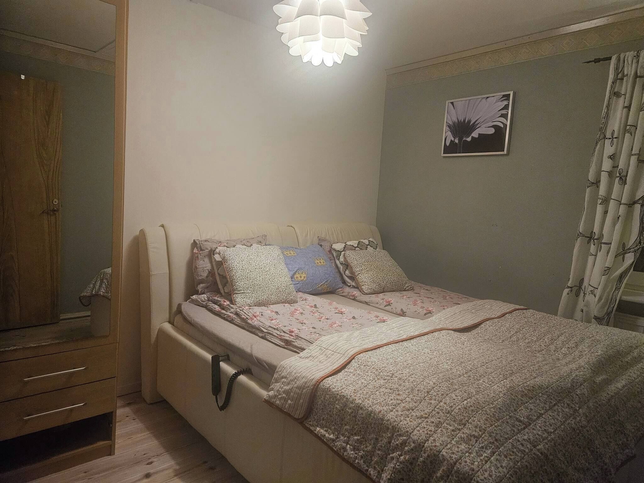 A bedroom with a bed, a wardrobe, a bedside table, and a wall-mounted light fixture.