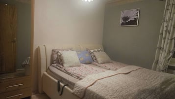 A bedroom with a bed, a wardrobe, a bedside table, and a wall-mounted light fixture.