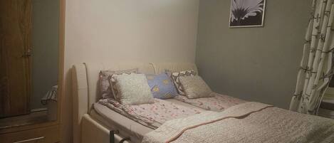 A bedroom with a bed, a wardrobe, a bedside table, and a wall-mounted light fixture.