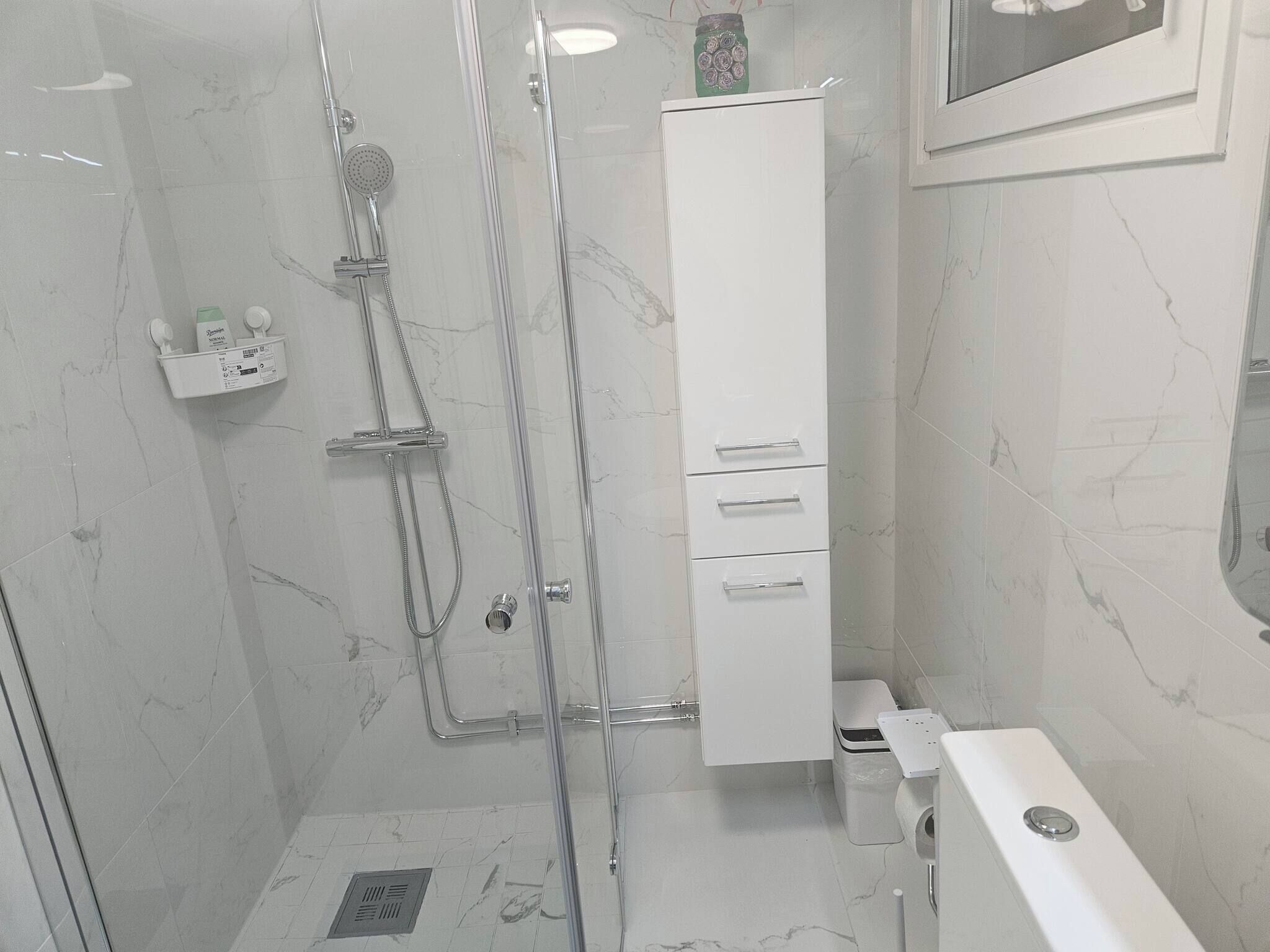 Ein modernes Badezimmer mit einer Duschkabine aus Glas, einem weißen Schrank und einer Toilette.