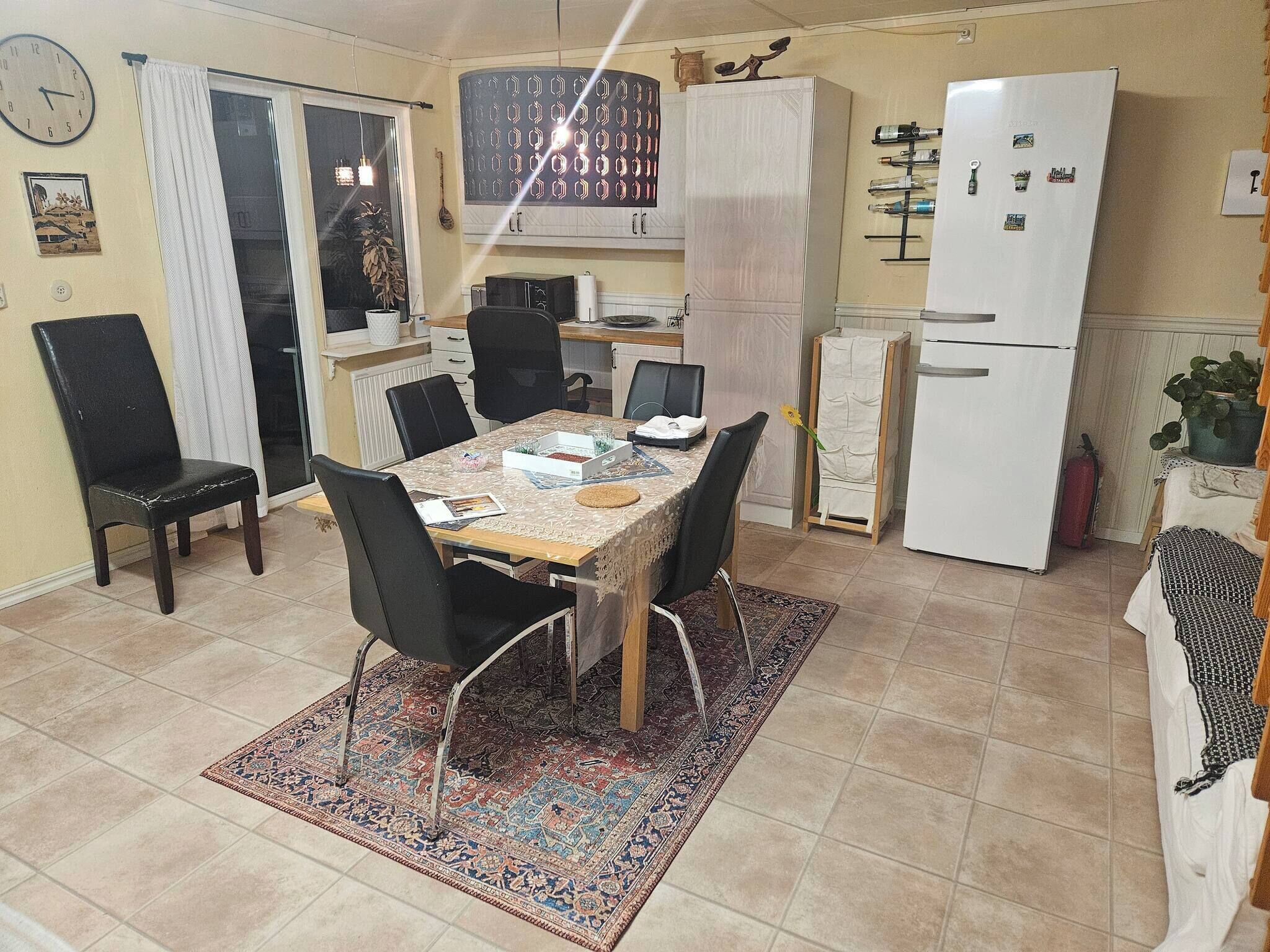 Ein Essbereich mit Tisch, Stühlen, einem gemusterten Teppich, einem Kühlschrank und einer Küchenarbeitsplatte.