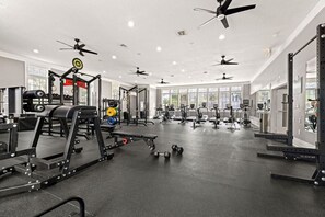 Ett rymligt gym med takfläktar, olika typer av träningsutrustning och stora fönster som släpper in naturligt ljus.