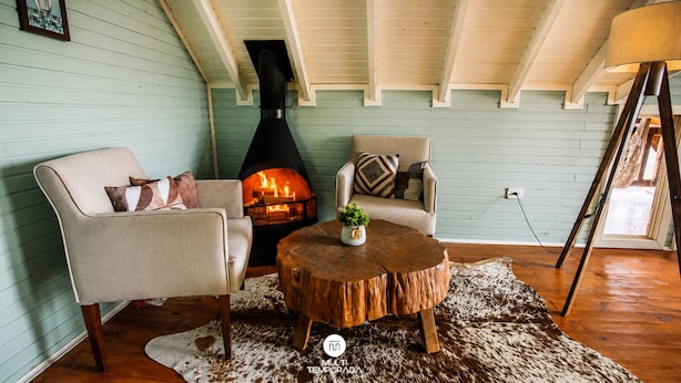 A cozy room with a fireplace, two chairs, a round wooden table, and a shaggy rug.