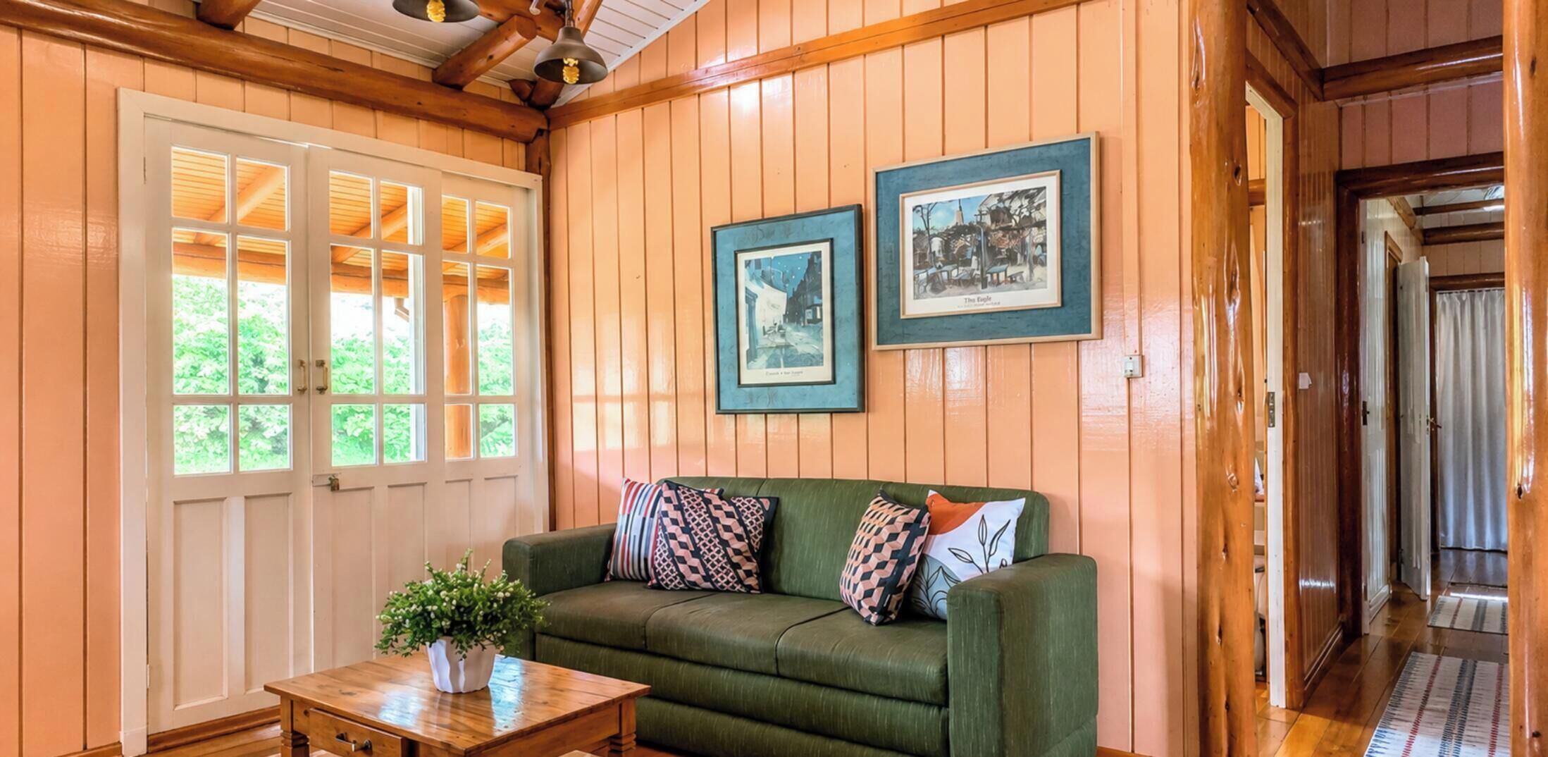 Une pièce chaleureuse avec un canapé vert, une petite table sur laquelle est posée une plante, et deux tableaux encadrés accrochés au mur.