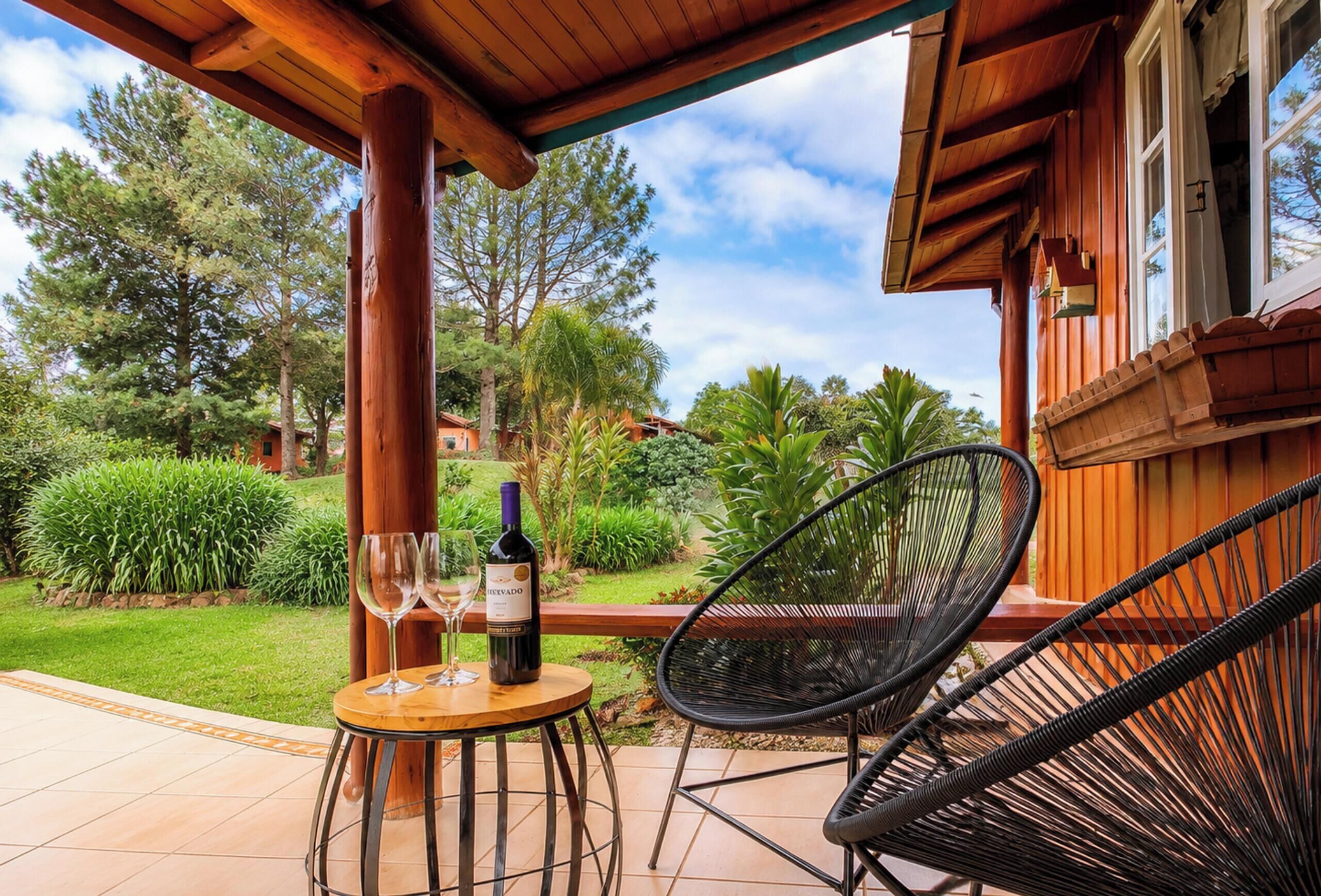 A wooden outdoor seating area with a table and chairs, a bottle of wine, and a glass.