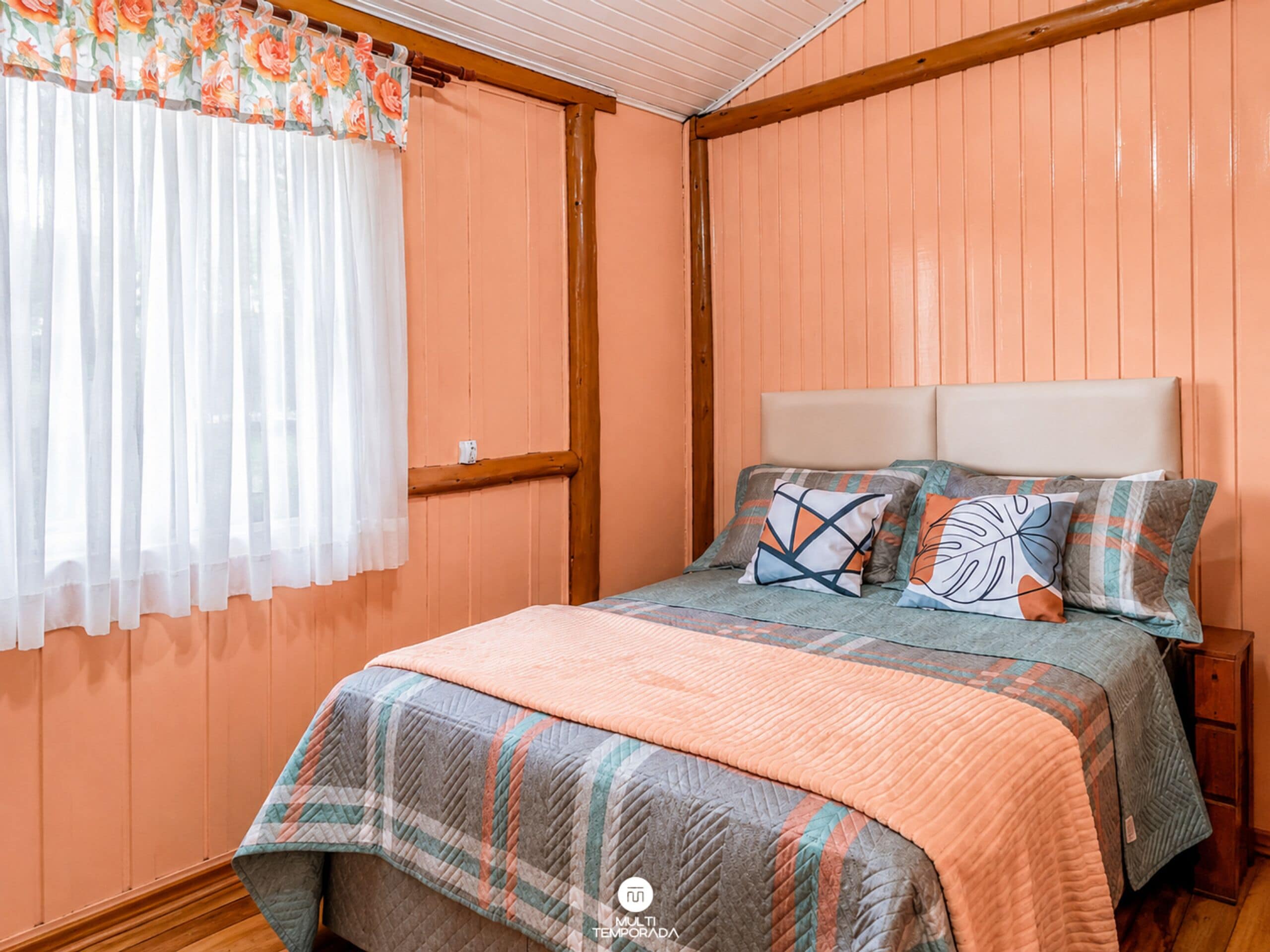 Ein Schlafzimmer mit einem Bett, Kissen, einem Fenster mit Vorhängen und einem hölzernen Kopfteil.