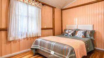 A bedroom with a bed, a window with sheer curtains, and wooden paneling on the walls.