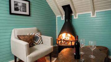 A cozy room with teal walls, a fireplace, a comfortable armchair, and a table with a bottle and glasses.
