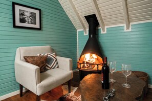 A cozy room with teal walls, a fireplace, a comfortable armchair, and a table with a bottle and glasses. - Cabanas do Perau - Alfredo Wagner-SC (Alfredo Wagner)