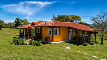 Uma casa térrea com telhado de telhas vermelhas, varanda e um pequeno jardim.