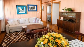 A cozy room with a sofa, a dining table with a floral centerpiece, and a wooden cabinet with glassware.